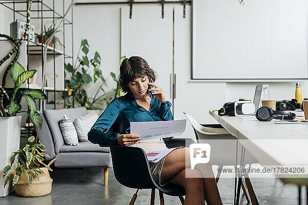 Young businesswoman with documents talking on smart phone in office