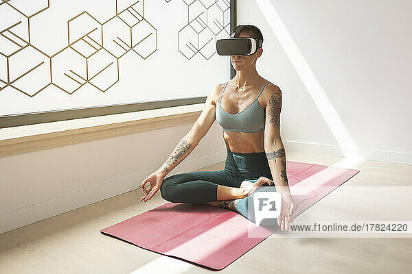 Woman practicing lotus position on mat wearing virtual reality headset in studio