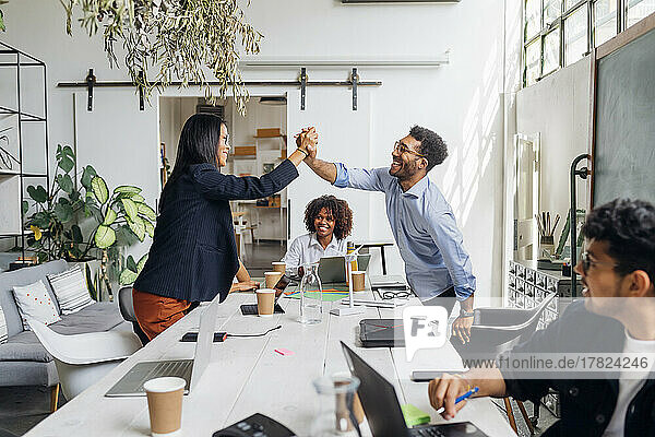 Happy businessman and businesswoman giving high-five over desk in office