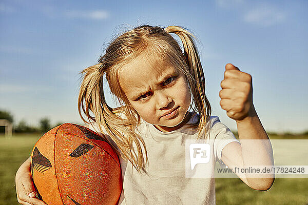 Blond girl holding rugby ball gesturing fist on sunny day