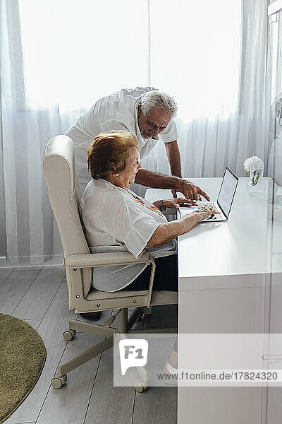 Man explaining laptop to senior woman at home