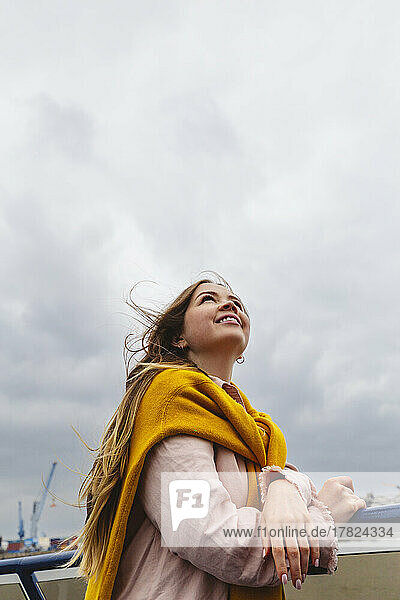 Smiling young woman standing under cloudy sky