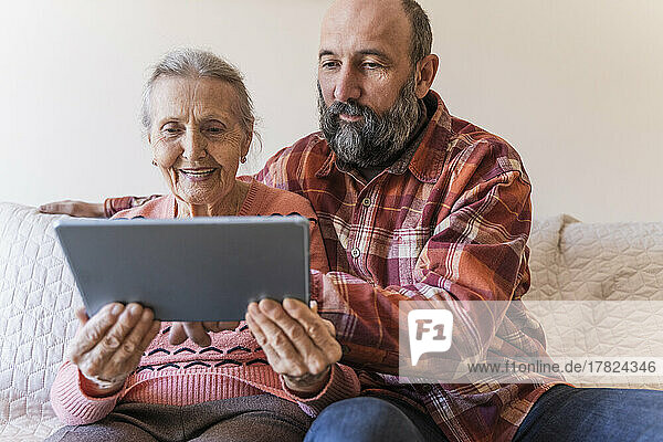 Man teaching tablet PC to senior woman at home