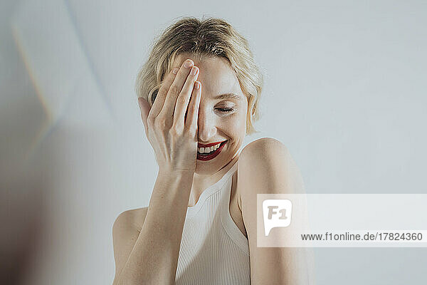 Shy woman covering eye with hand against white background