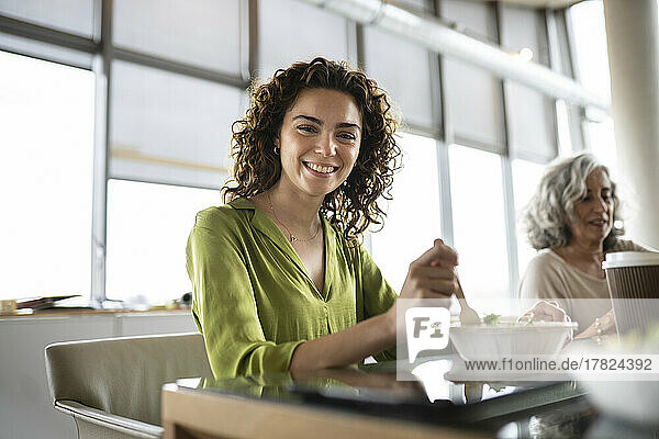 Smiling businesswoman with bowl of salad sitting at desk