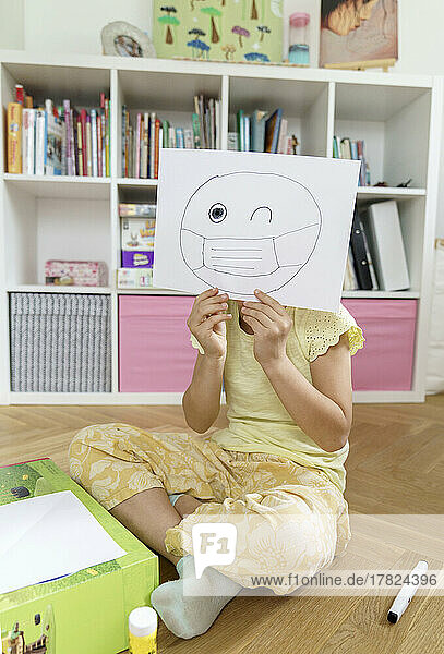 Mädchen hält Papier mit Emoticon-Zeichnung zu Hause