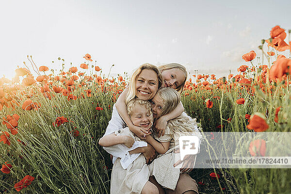 Happy mother and daughters embracing each other in poppy field