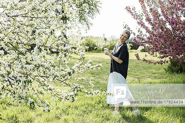 Happy woman holding white flowers standing in garden