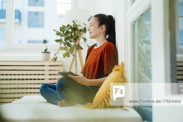 Thoughtful woman with tablet PC in living room