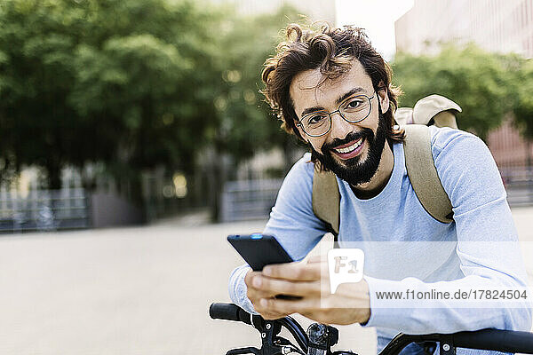 Smiling man with bicycle using mobile phone