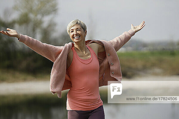 Smiling mature woman with arms outstretched enjoying sunny day