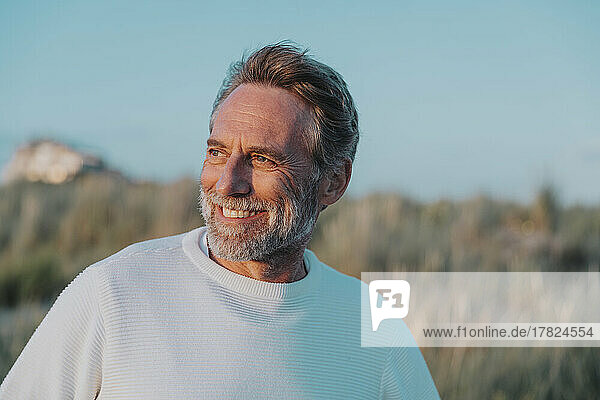 Happy mature man with beard looking away at beach