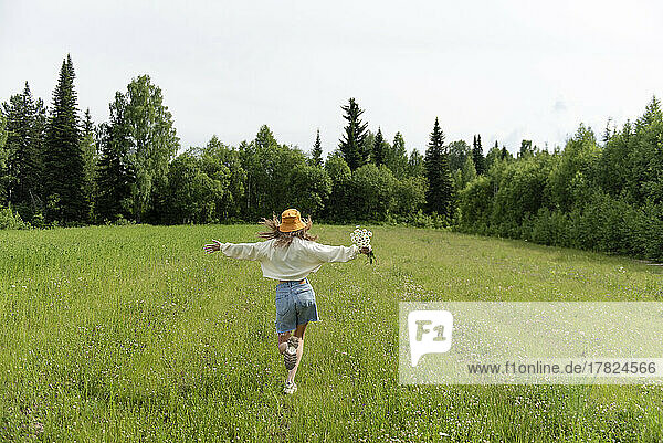 Woman with chamomile flowers running on grass