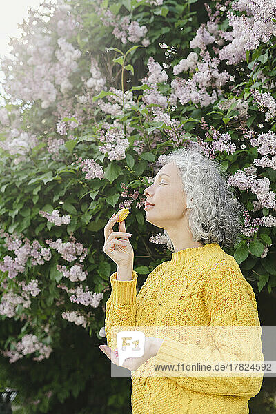 Woman with eyes closed eating macaroon under lilac tree at park