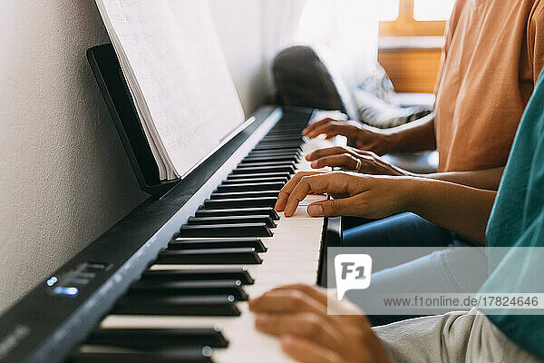 Hands of woman and girl playing piano at home