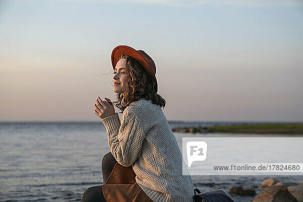 Lächelnde junge Frau mit Hut genießt den Sonnenuntergang