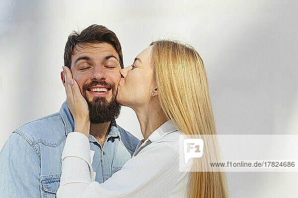 Affectionate blond woman kissing man on cheek in front of wall