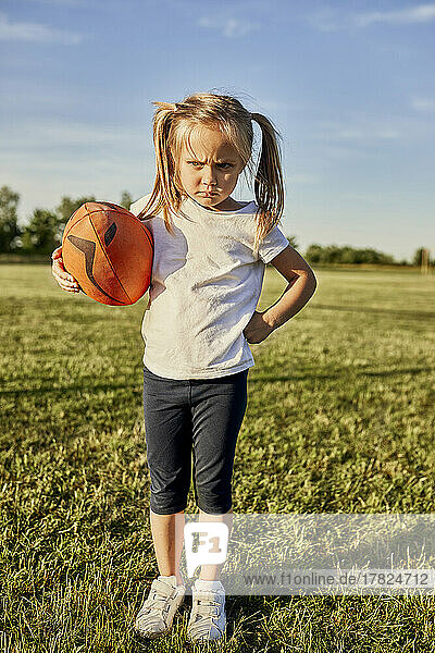 Angry blond girl with rugby ball standing at sports field on sunny day