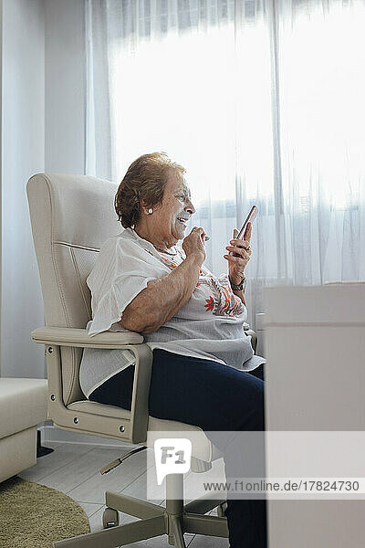 Glückliche ältere Frau  die zu Hause ihr Mobiltelefon benutzt