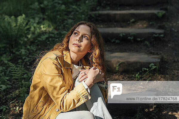 Contemplative woman sitting on step in forest
