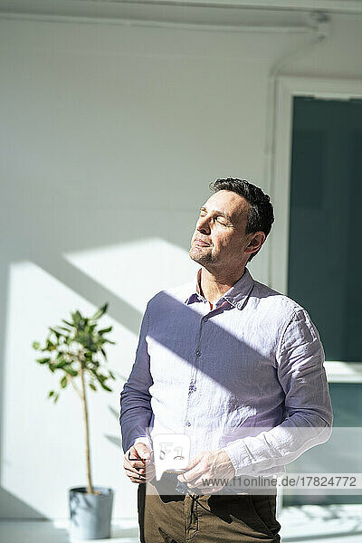 Businessman with eyes closed sunbathing at office