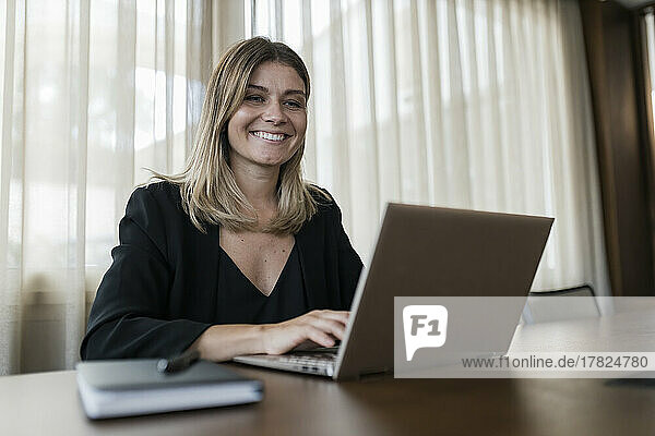 Smiling businesswoman using laptop on table at hotel