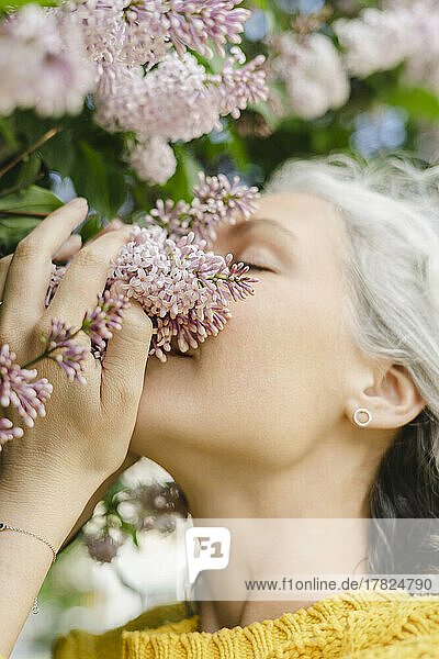Beautiful woman smelling lilac flowers of tree at park