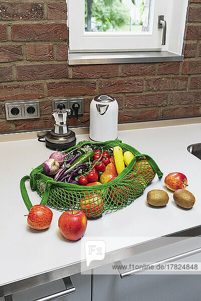 Fresh fruits and vegetables in reusable shopping bag on kitchen counter at home