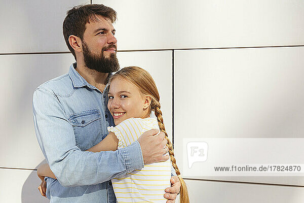 Happy girl embracing father in front of wall