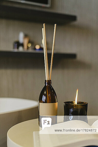 Incense sticks by burning scented candle on table in bathroom