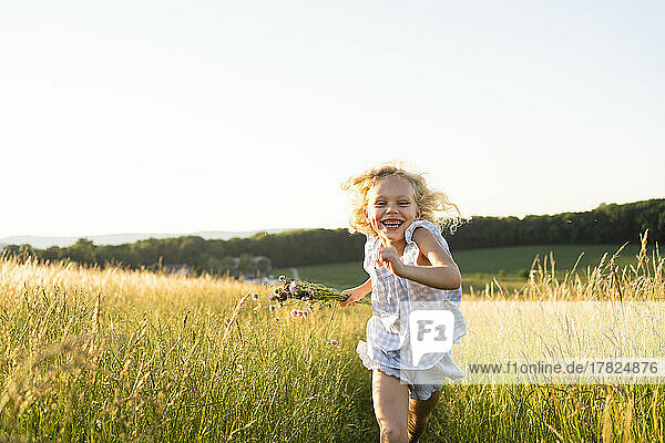 Fröhliches Mädchen läuft an einem sonnigen Tag im Feld