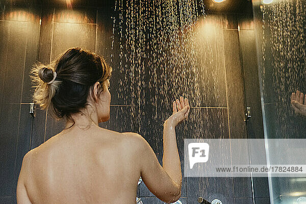 Woman touching water drops from shower in bathroom