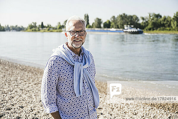 Smiling senior man wearing eyeglasses standing at riverbank