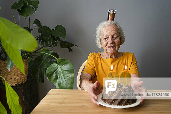 Lächelnde ältere Frau  die zu Hause Geburtstag mit Kuchen feiert