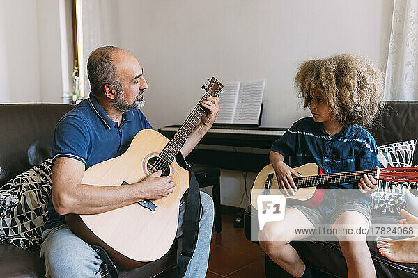 Man teaching son to play guitar at home