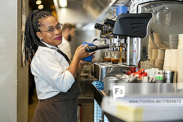 Smiling barista using coffee maker at restaurant kitchen