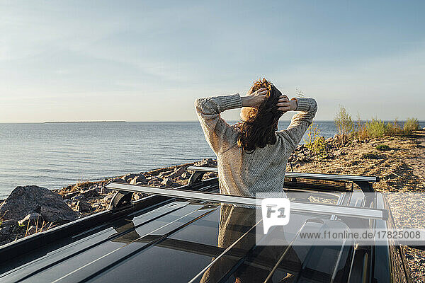 Junge Frau mit den Händen hinter dem Kopf genießt die Brise durch das Sonnendach des Autos