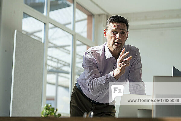 Businessman gesturing leaning on table at office