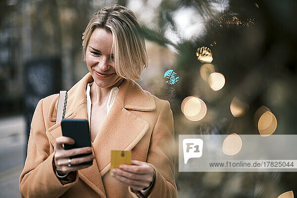 Smiling woman using credit card to make payment through smart phone