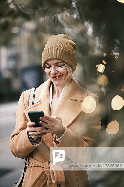 Happy woman wearing knit hat using mobile phone
