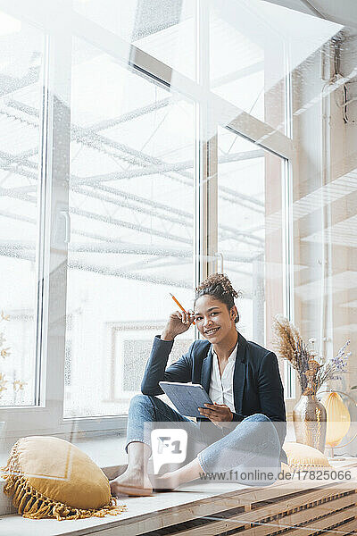 Happy businesswoman with digital tablet PC sitting in front of window
