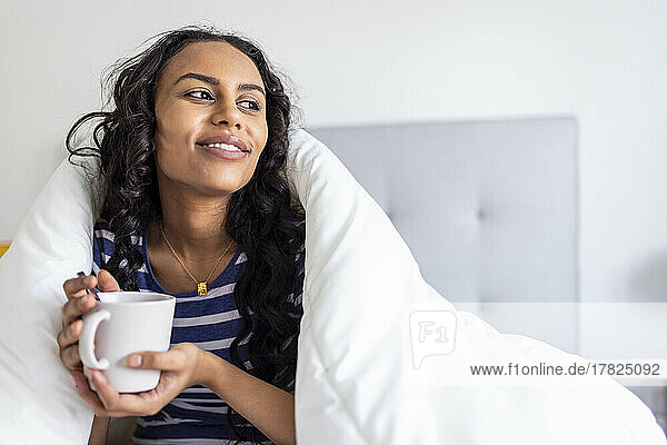 Thoughtful woman enjoying coffee under blanket