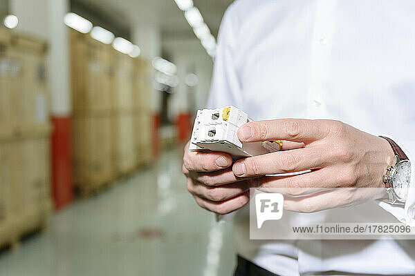 Hands of businessman holding electronic part in factory