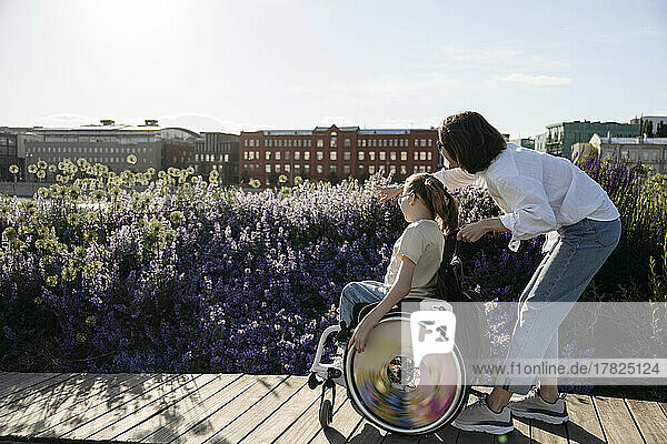 Woman pointing at flowers to daughter with disability on sunny day