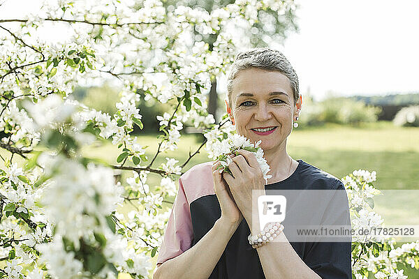 Smiling woman holding white flower standing in garden