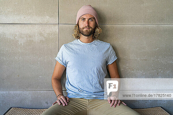 Man wearing knit hat sitting in front of wall
