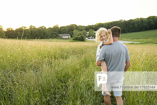 Father carrying smiling daughter at field