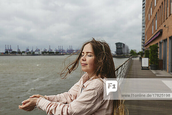Lächelnde Frau mit geschlossenen Augen steht am Hamburger Hafen