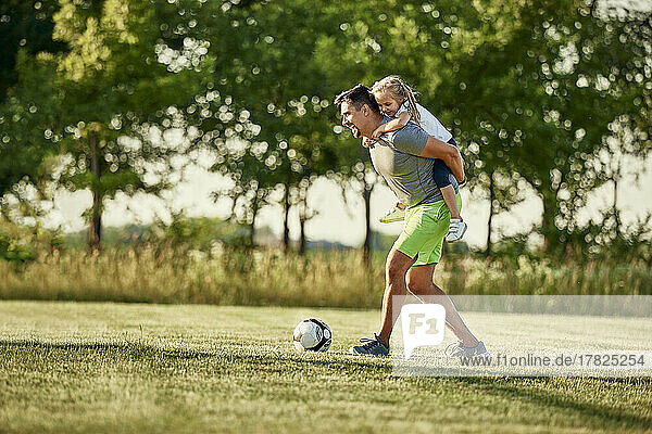 Happy girl enjoying piggyback ride given by man playing soccer at sports field
