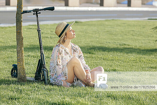 Reife Frau sitzt am Tretroller und genießt den sonnigen Tag im Park